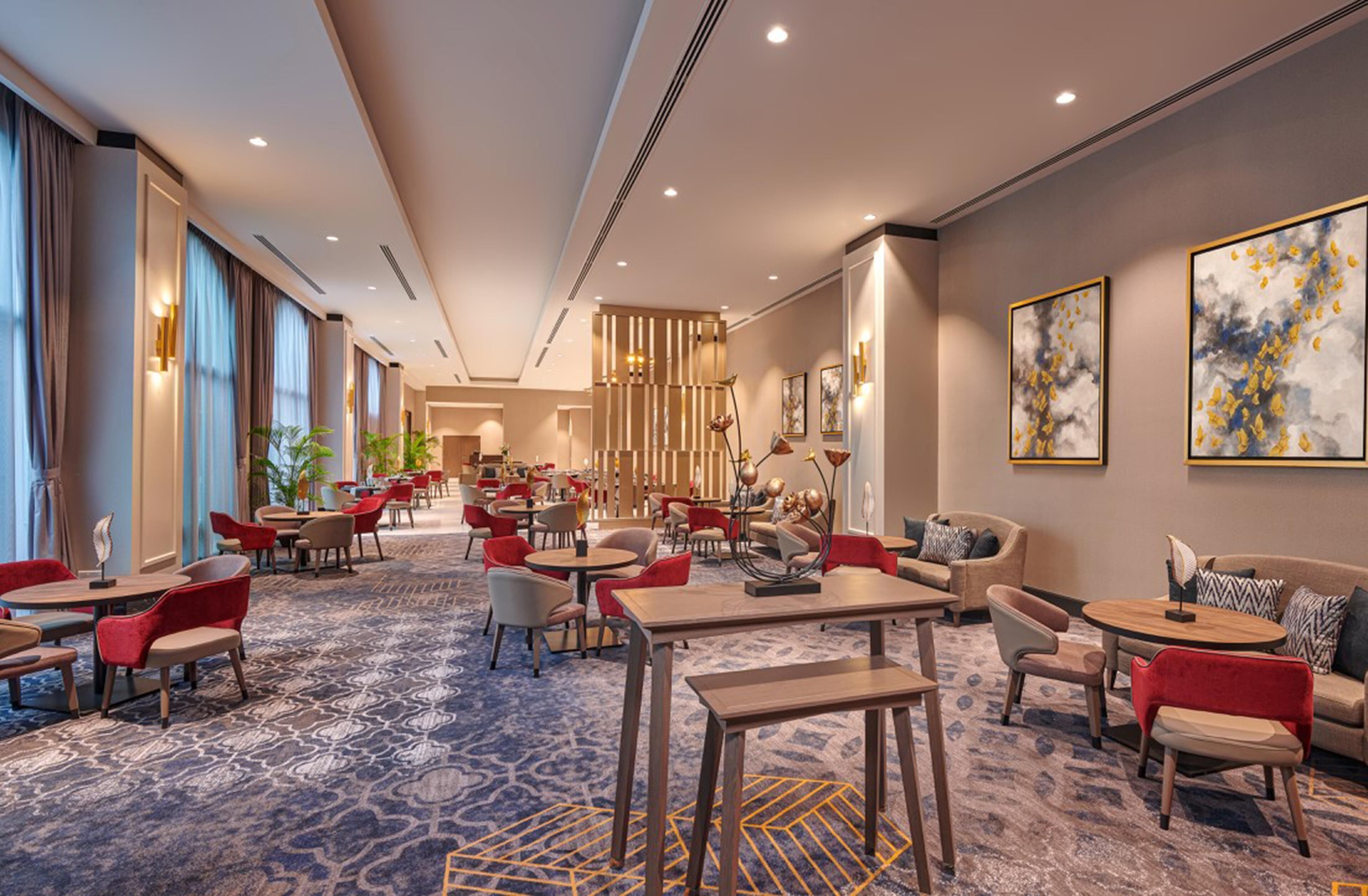 A hotel lobby with a patterned carpet, red and beige seating, and artwork on the walls.