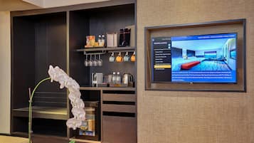 A hotel room with a television displaying room options, a shelf with toiletries, and a potted orchid.