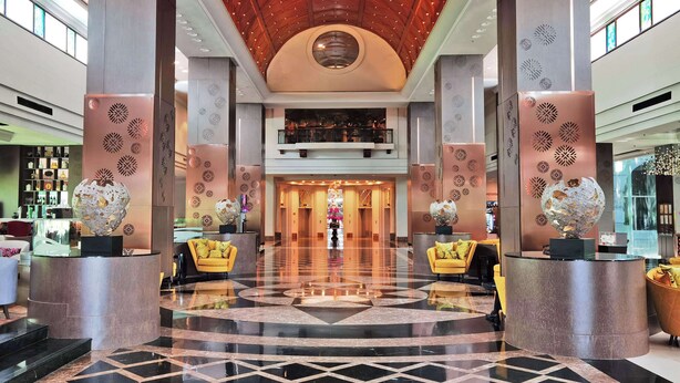 Eine großzügige Lobby mit hoher Decke, markanten Säulen und einem zentralen, runden Oberlicht.