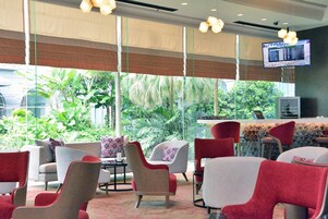 A restaurant with a bar area, red and grey chairs, and large windows with a view of greenery.