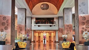 Eine großzügige Lobby mit hoher Decke, einem zentralen Kronleuchter und einem polierten Marmorboden.
