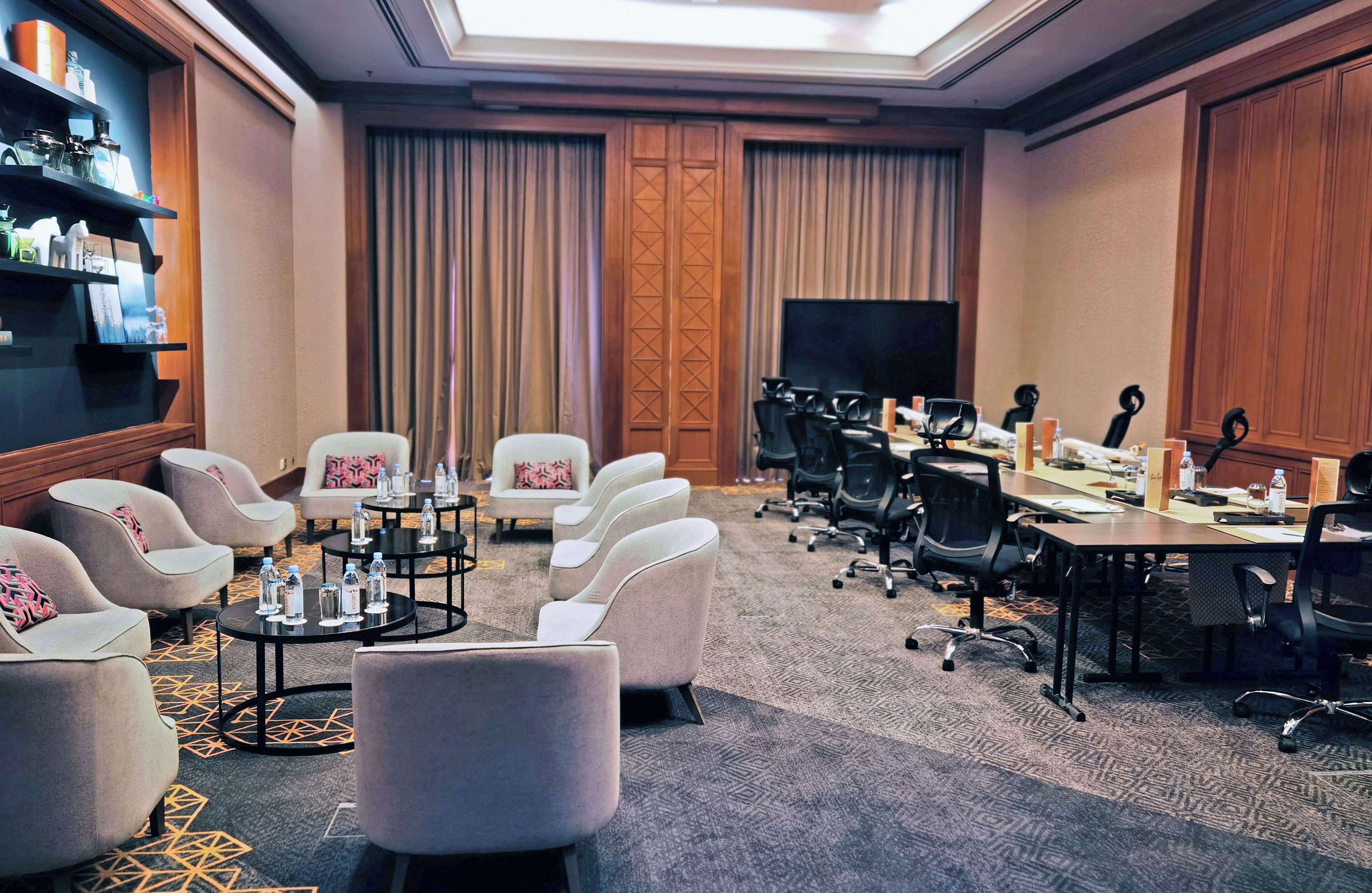 Uma sala de conferências com uma mesa comprida, várias cadeiras, uma televisão e uma estante com objetos.