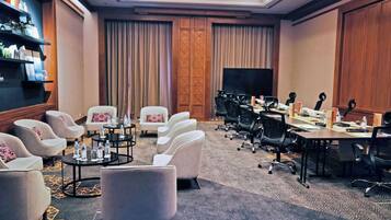 Uma sala de conferências com uma mesa comprida, várias cadeiras, uma televisão e uma estante com objetos.