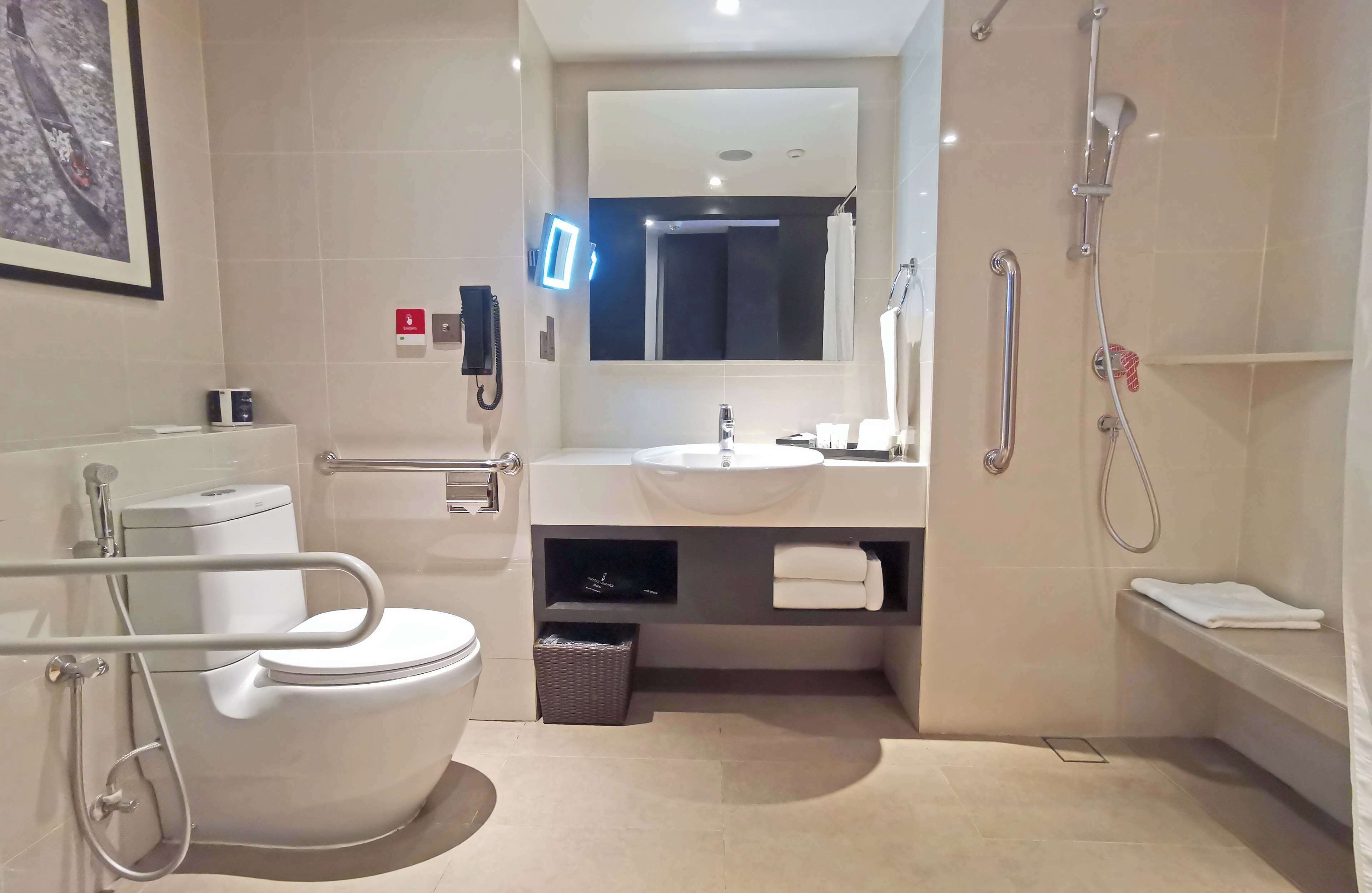 A modern bathroom with a toilet, sink, mirror, shower, and a telephone.