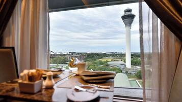 Mesa de comedor con platos, cubiertos y salero, con vistas a una torre y vegetación.