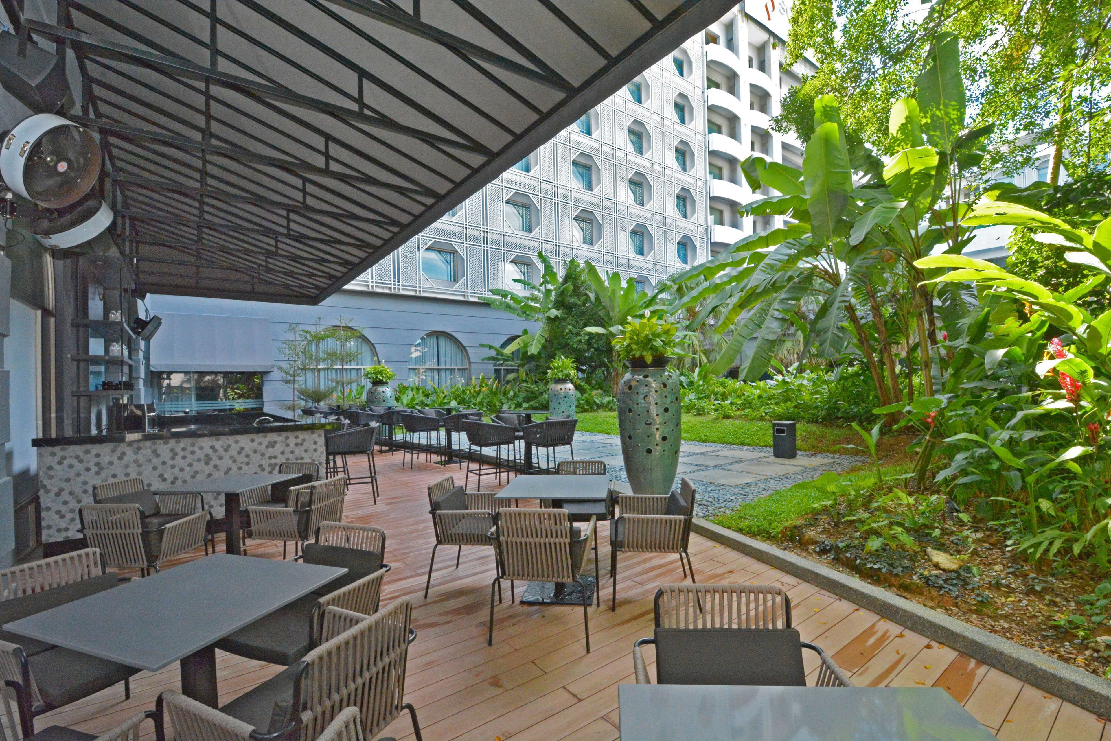 An outdoor patio with tables and chairs, a large planter, and a building in the background.