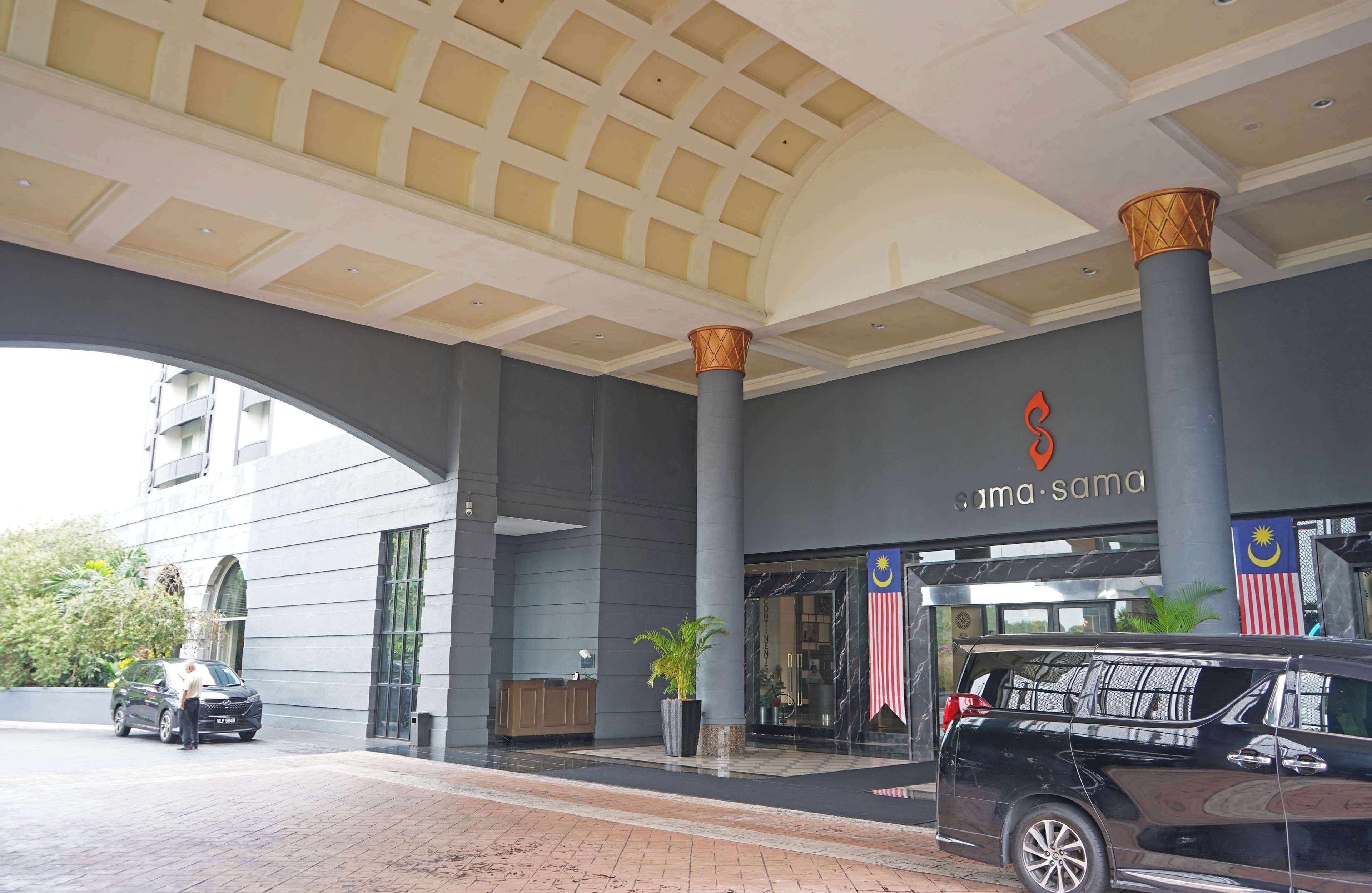 A hotel entrance with a large archway, a reception desk, and a parking area.
