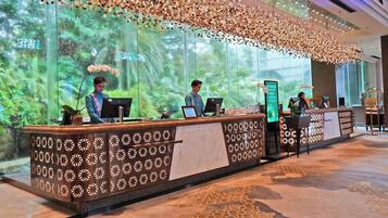 A reception desk with a patterned design, a large window with a view of greenery, and a decorative ceiling.