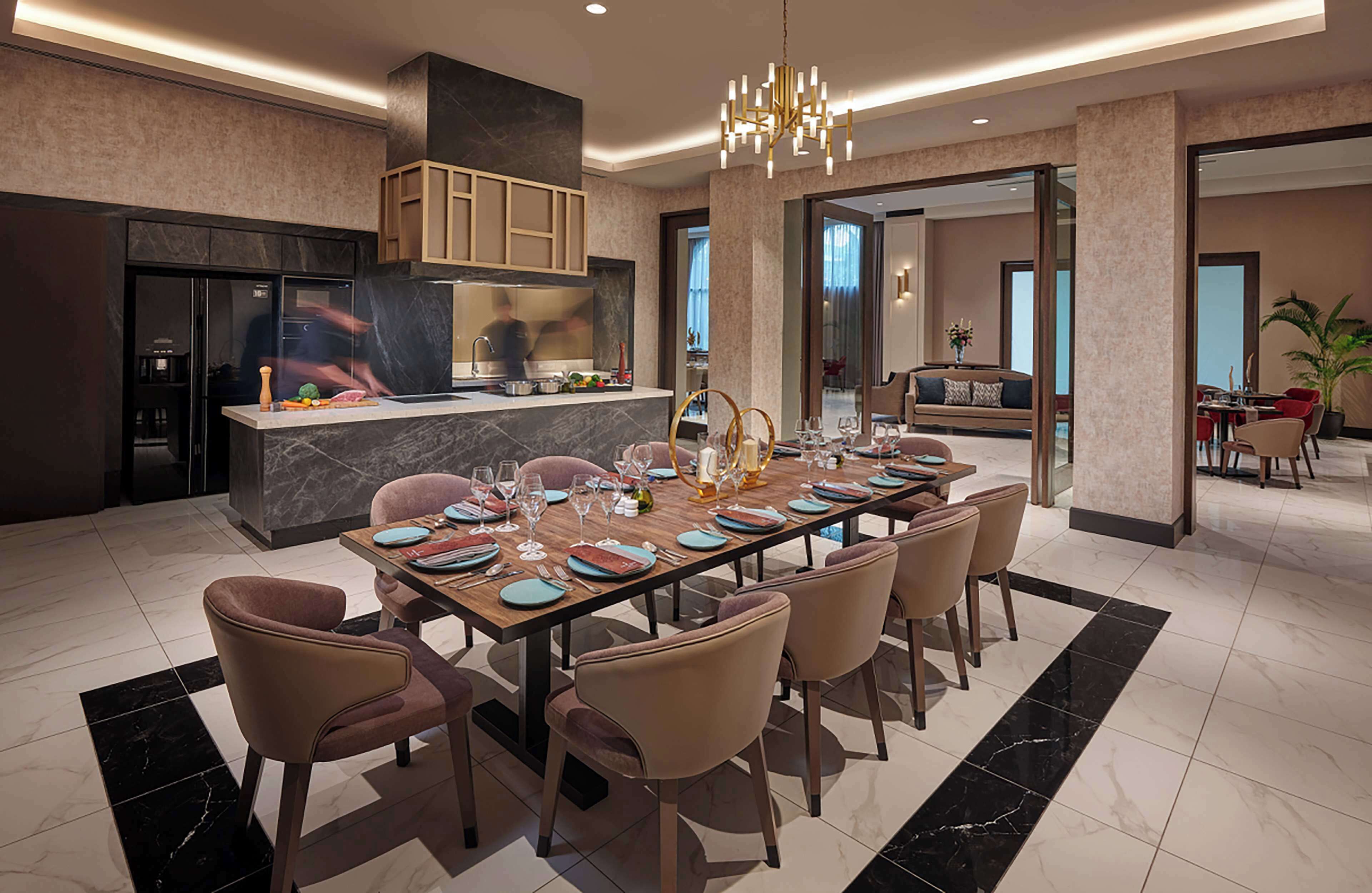 A modern kitchen with a marble countertop, a dining area with a long table set for six, and a living area with a sofa and a coffee table.