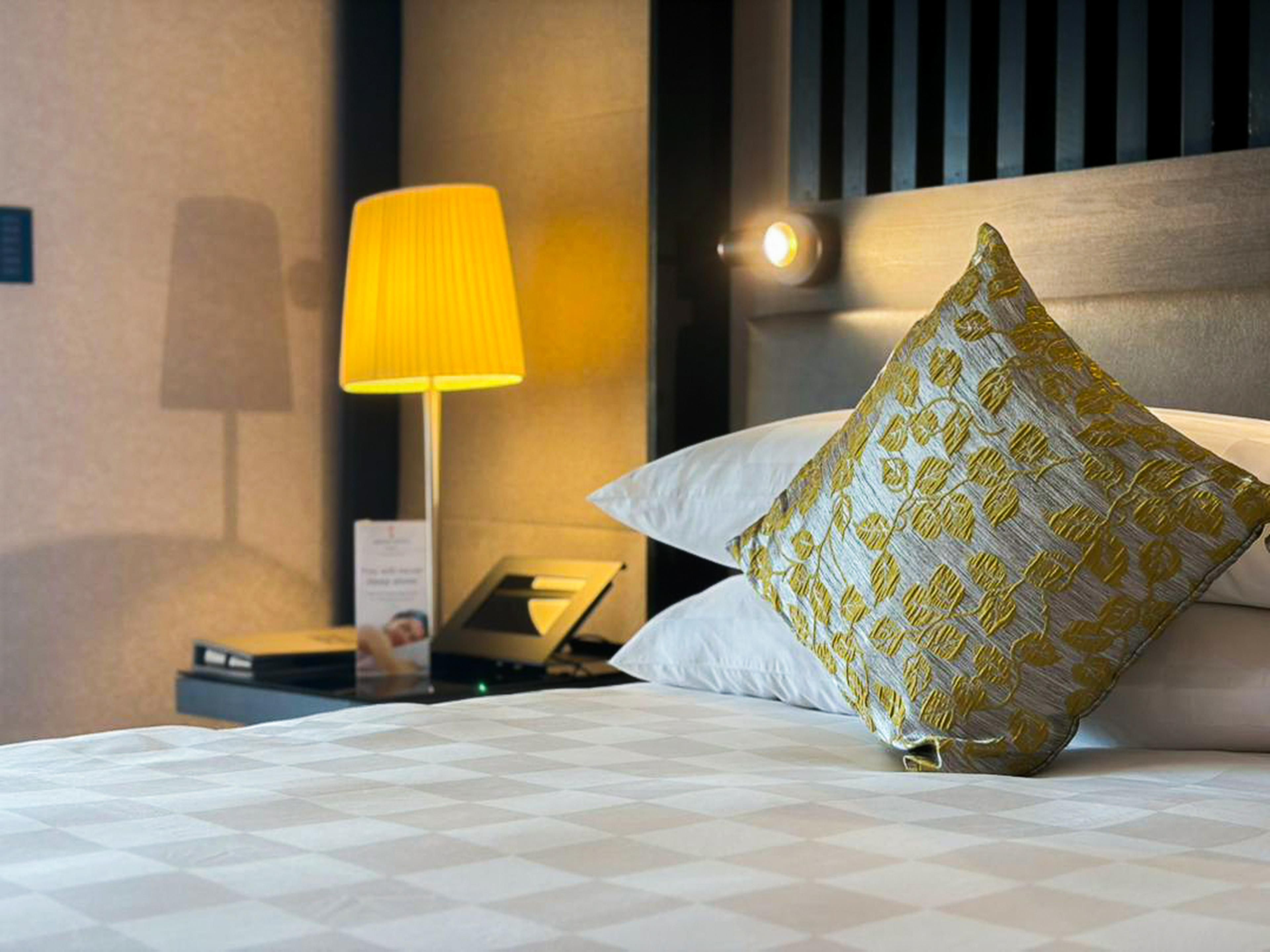 A hotel room with a bed, a nightstand, a lamp, and a pillow.