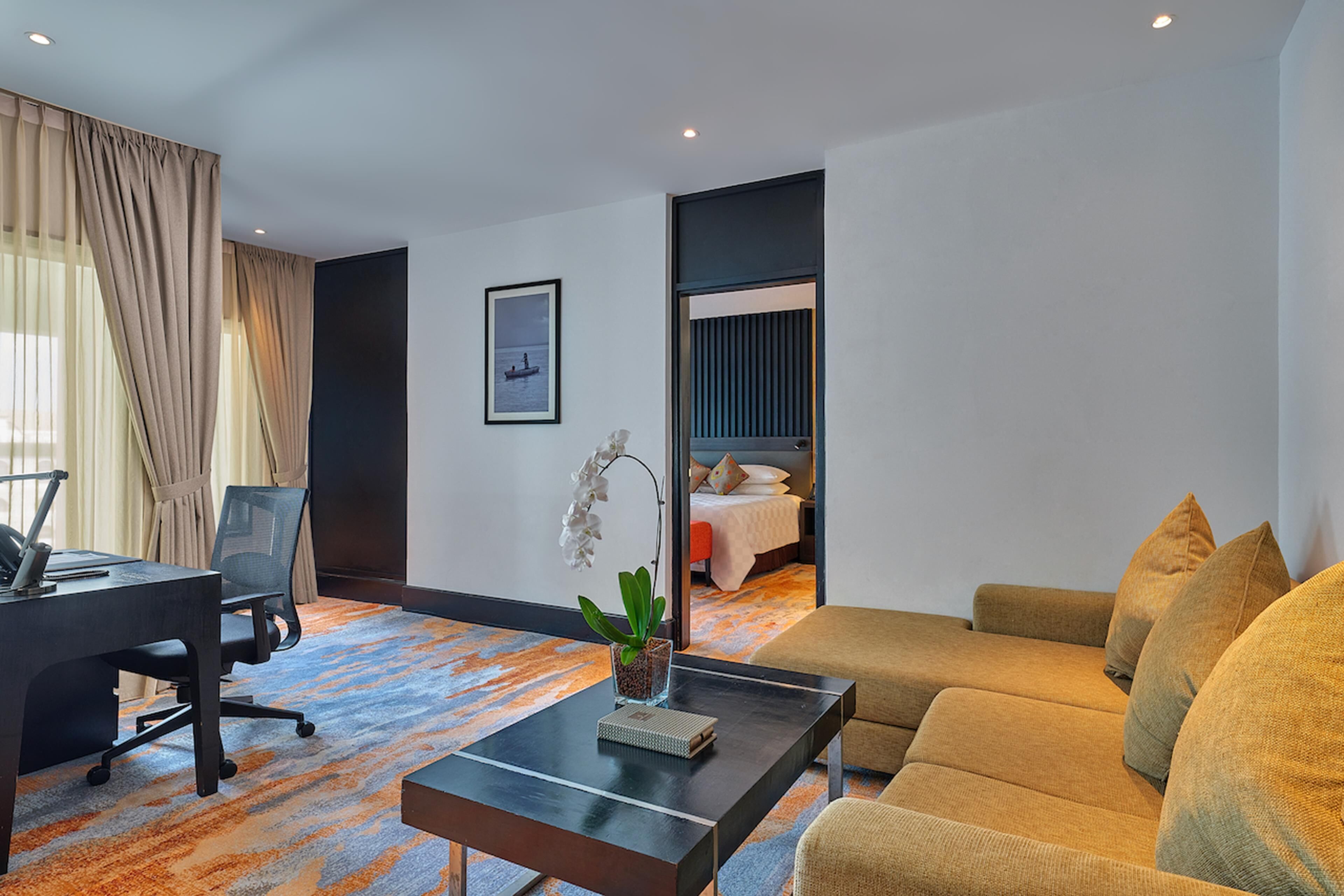 A hotel room with a desk, a sofa, a bed, and a view of the sea.