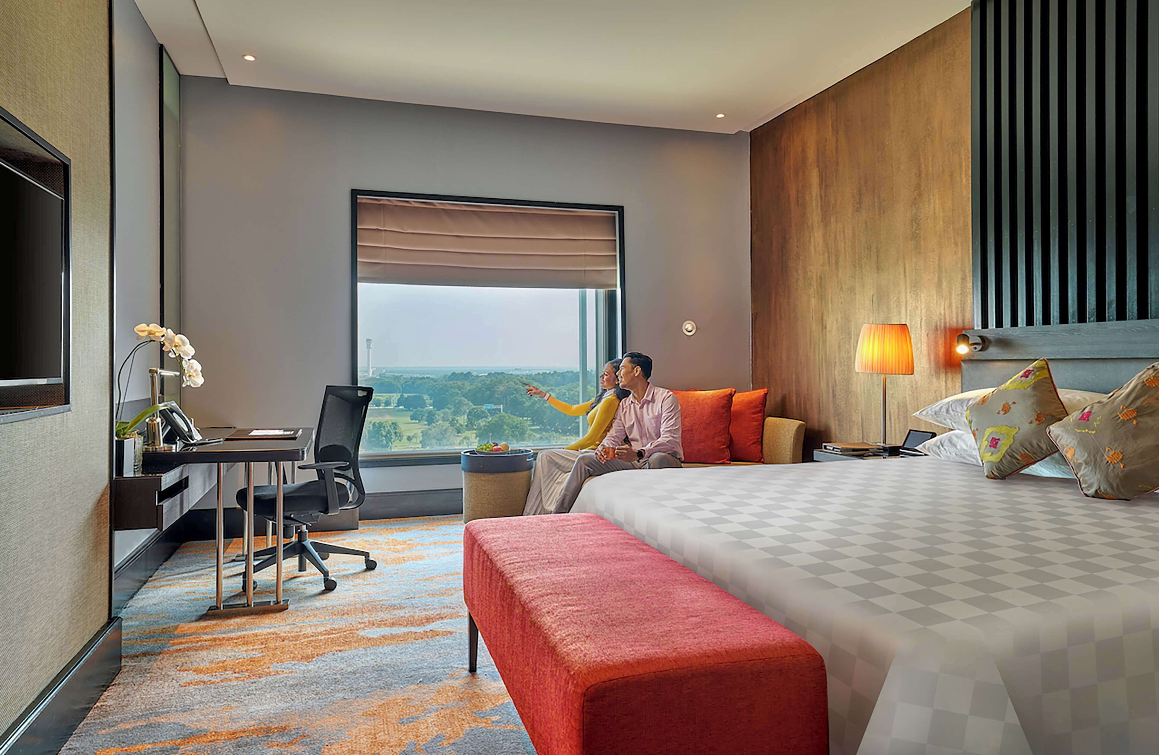 A hotel room with a large bed, a desk with a chair, a TV, and a view of the outdoors.