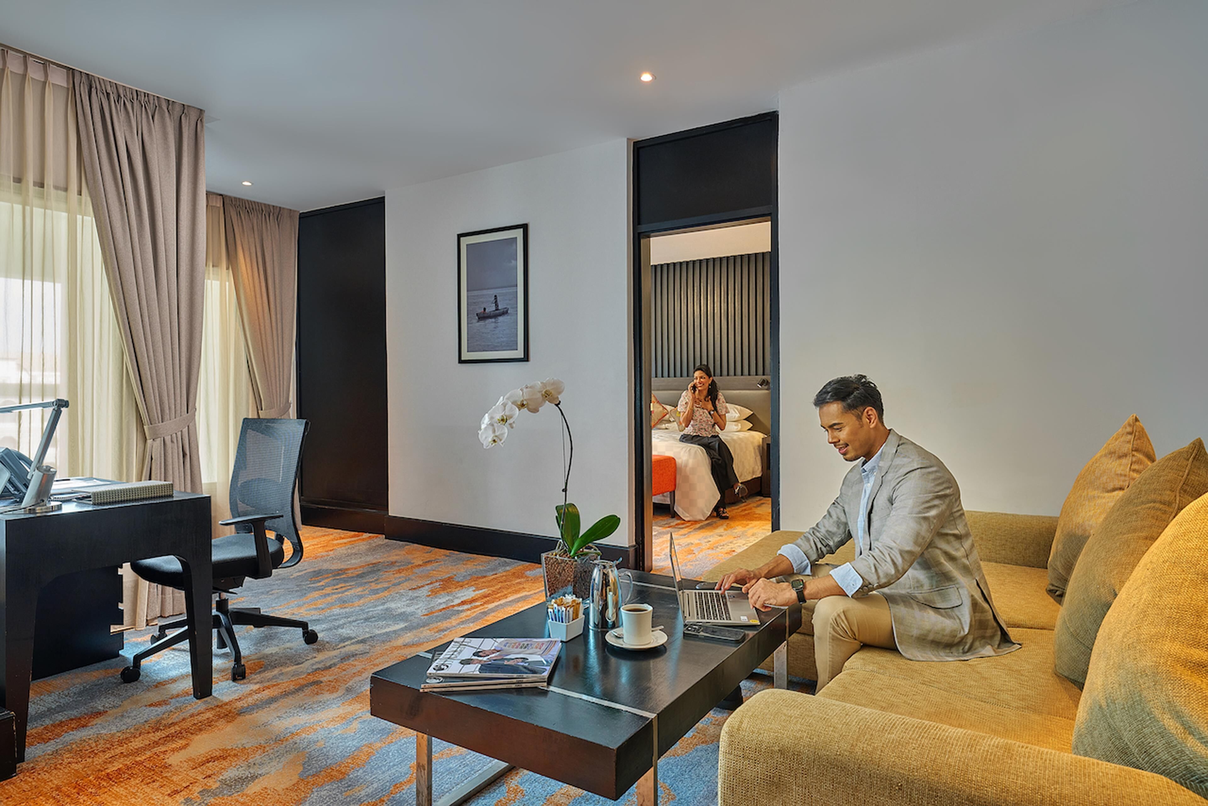 Quarto de hotel com uma escrivaninha, um laptop, um sofá e uma cama.