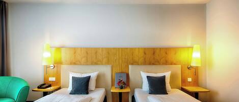 Habitación de hotel con dos camas, cabecera de madera, lámparas de noche, un teléfono y una mesita con un jarrón de flores.