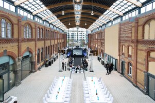 Un salón amplio con techos altos y ventanas arqueadas, que cuenta con un escenario central con una pantalla grande y asientos dispuestos en filas.
