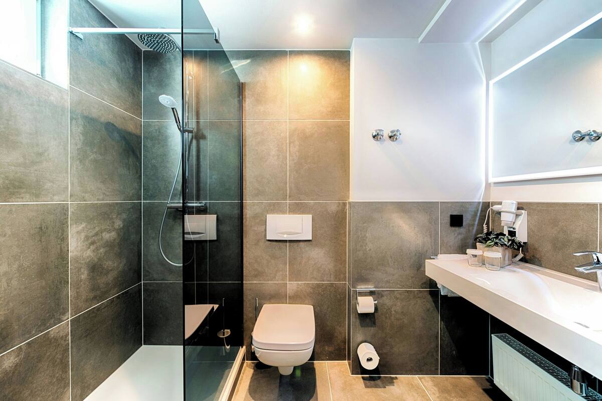 Une salle de bain moderne dotée d’une douche à parois de verre, de toilettes et d’un meuble-lavabo avec un évier et un miroir.