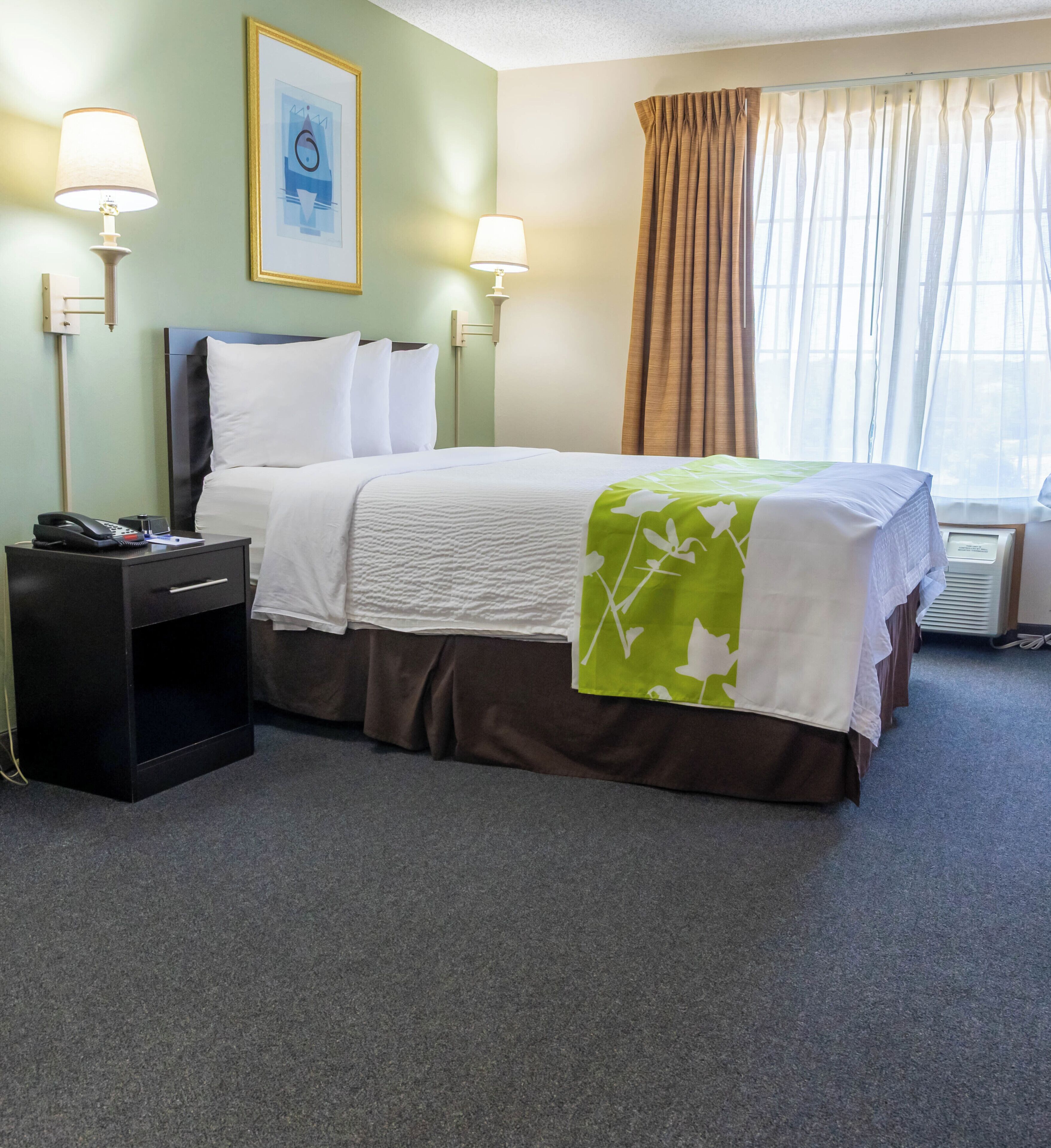 A hotel room with a bed, bedside lamps, a telephone, and a framed picture on the wall.