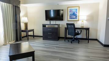 Habitación de hotel con televisor de pantalla plana, escritorio con silla, cómoda y mesita de noche.