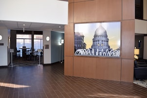 A lobby with a large wall-mounted painting of a capitol building, a reception desk, and a seating area with chairs.