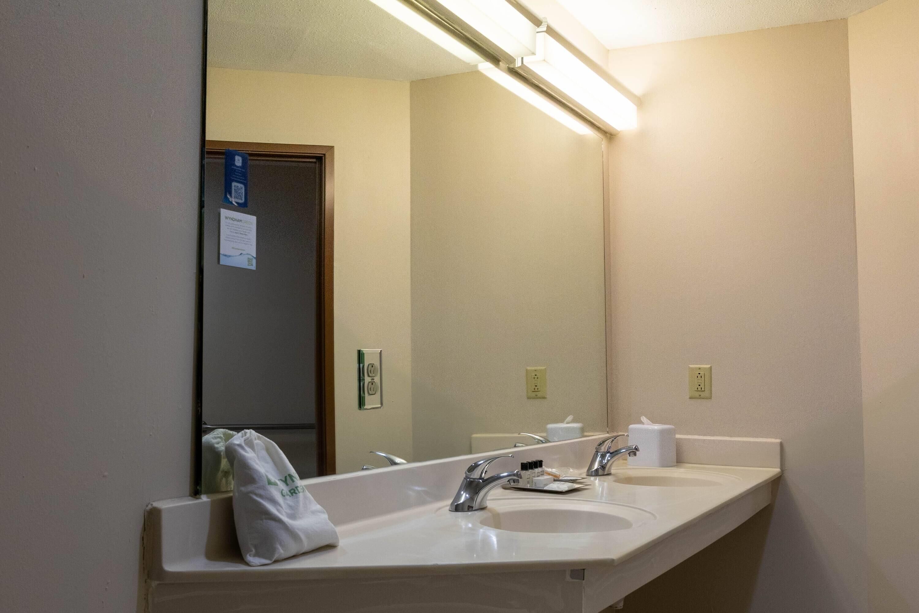A hotel bathroom with two sinks, a mirror, and a towel hanging on the wall.
