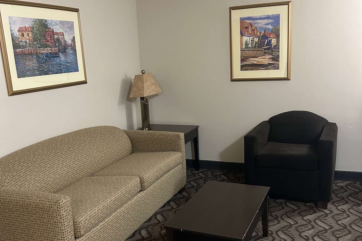 A room with a beige sofa, a black armchair, a small table, and two framed paintings on the wall.