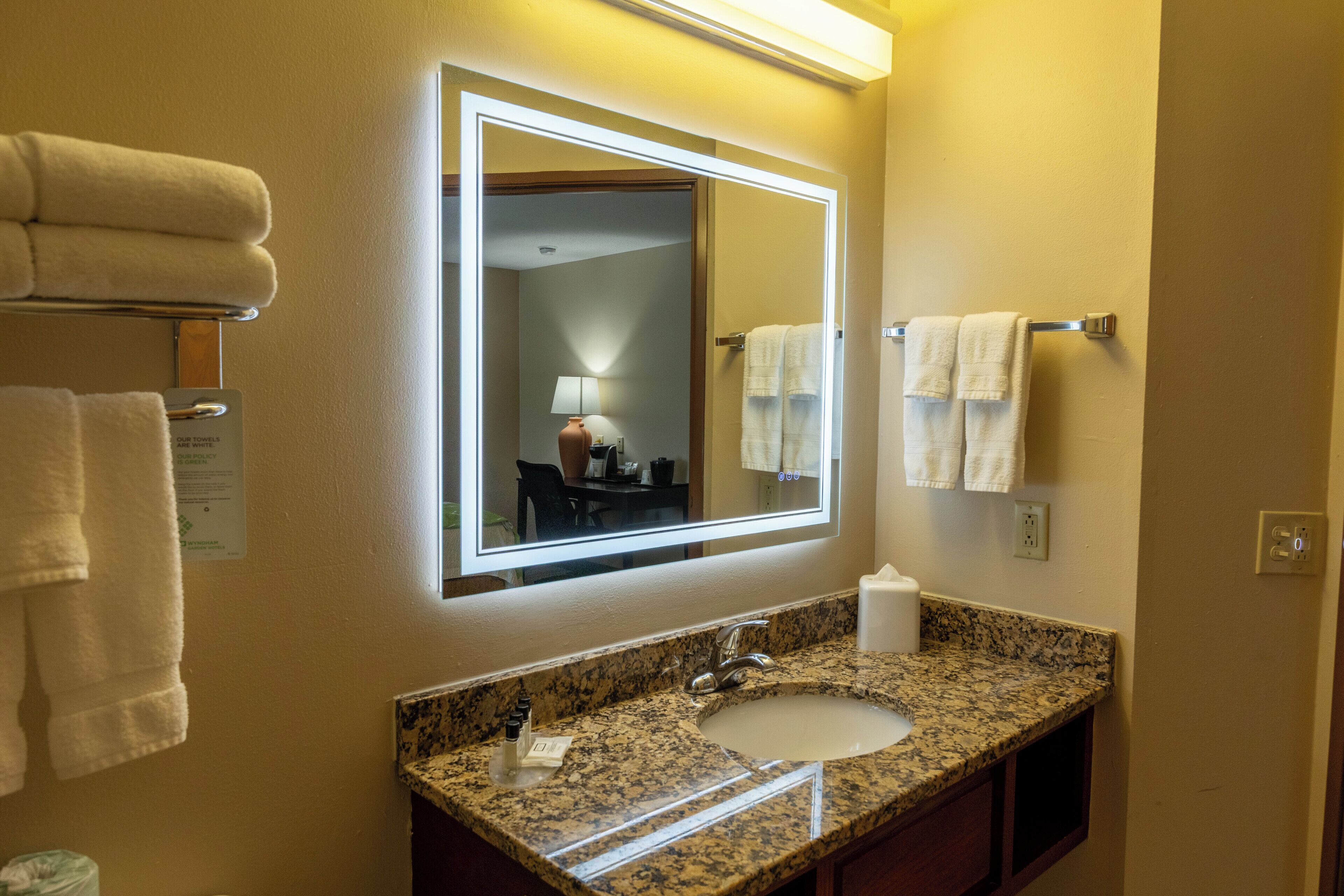 A hotel bathroom with a granite countertop sink, a mirror, and two white towels on towel racks.
