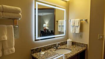 A hotel bathroom with a granite countertop sink, a mirror, and two white towels on towel racks.