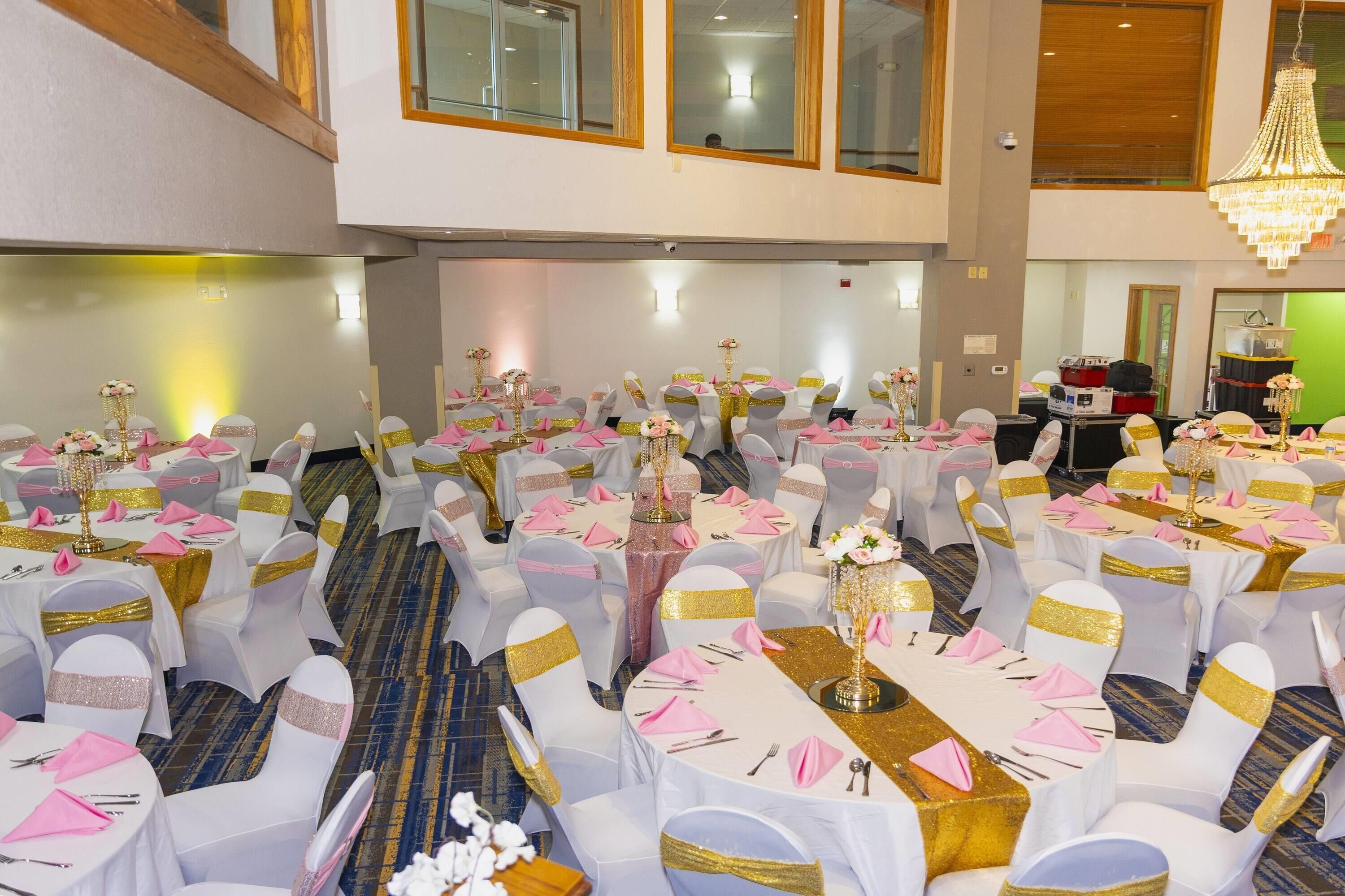 A banquet hall with round tables, white chairs with gold sashes, and a chandelier.