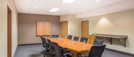 A conference room with a long table, black chairs, a whiteboard, and a sink.