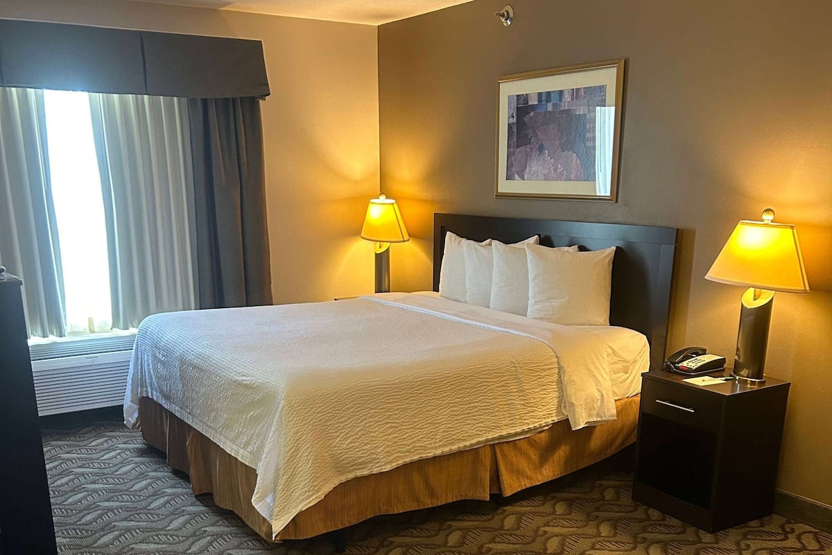 A hotel room with a large bed, two bedside lamps, a framed picture on the wall, and a window with curtains.