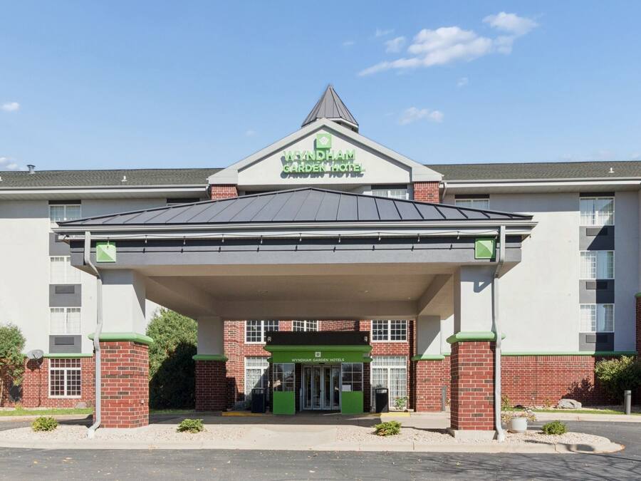 A hotel with a covered entrance, a green and white color scheme, and a brick facade.