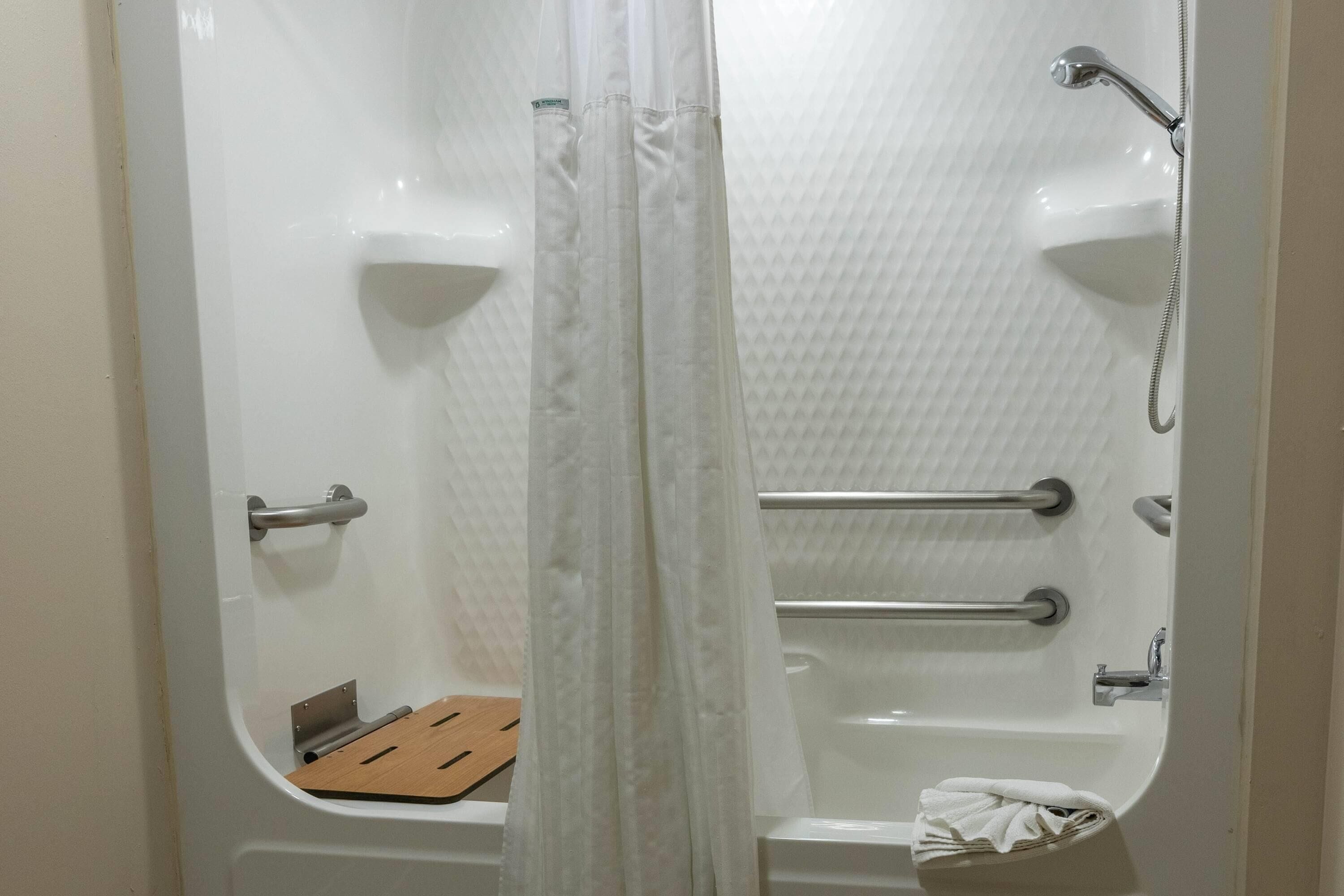 Une salle de bain équipée d’une baignoire, d’un rideau de douche, de barres d’appui et d’une étagère en bois.