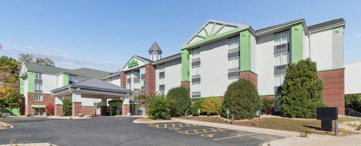Un hotel de varios pisos con entrada cubierta, fachada de ladrillo y detalles en verde.