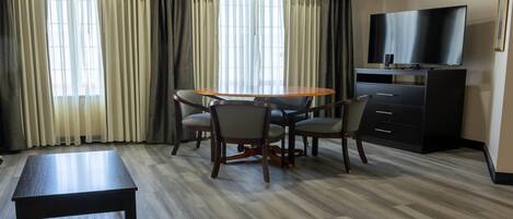 Een hotelkamer met een eettafel, stoelen, een bankje, een televisie en een kast.