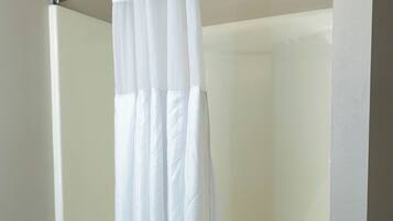A bathroom with a white shower curtain, a bathtub, and a toilet.