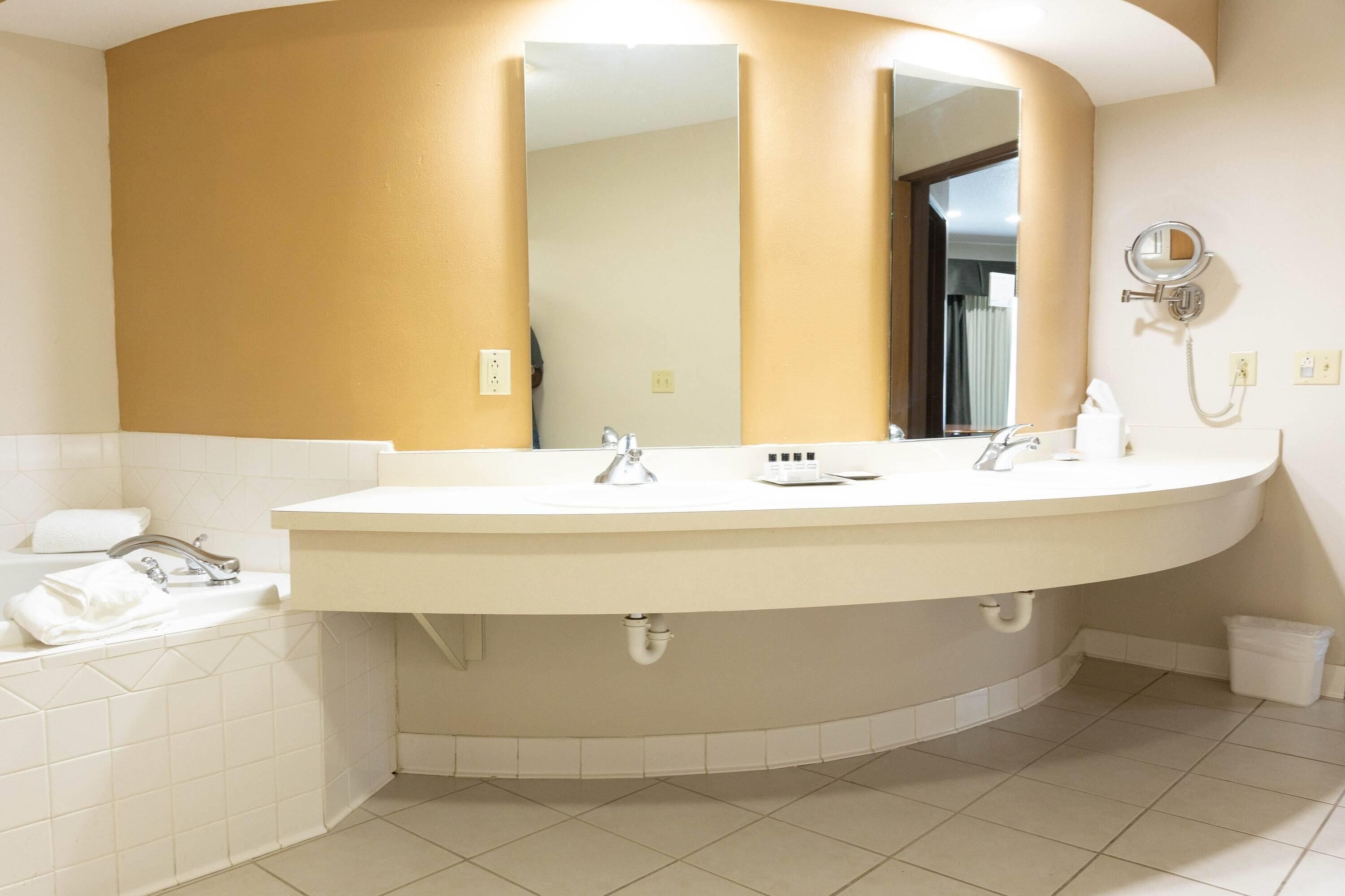 Une salle de bain avec un grand lavabo incurvé, deux robinets, un miroir et un sèche-cheveux fixé au mur.