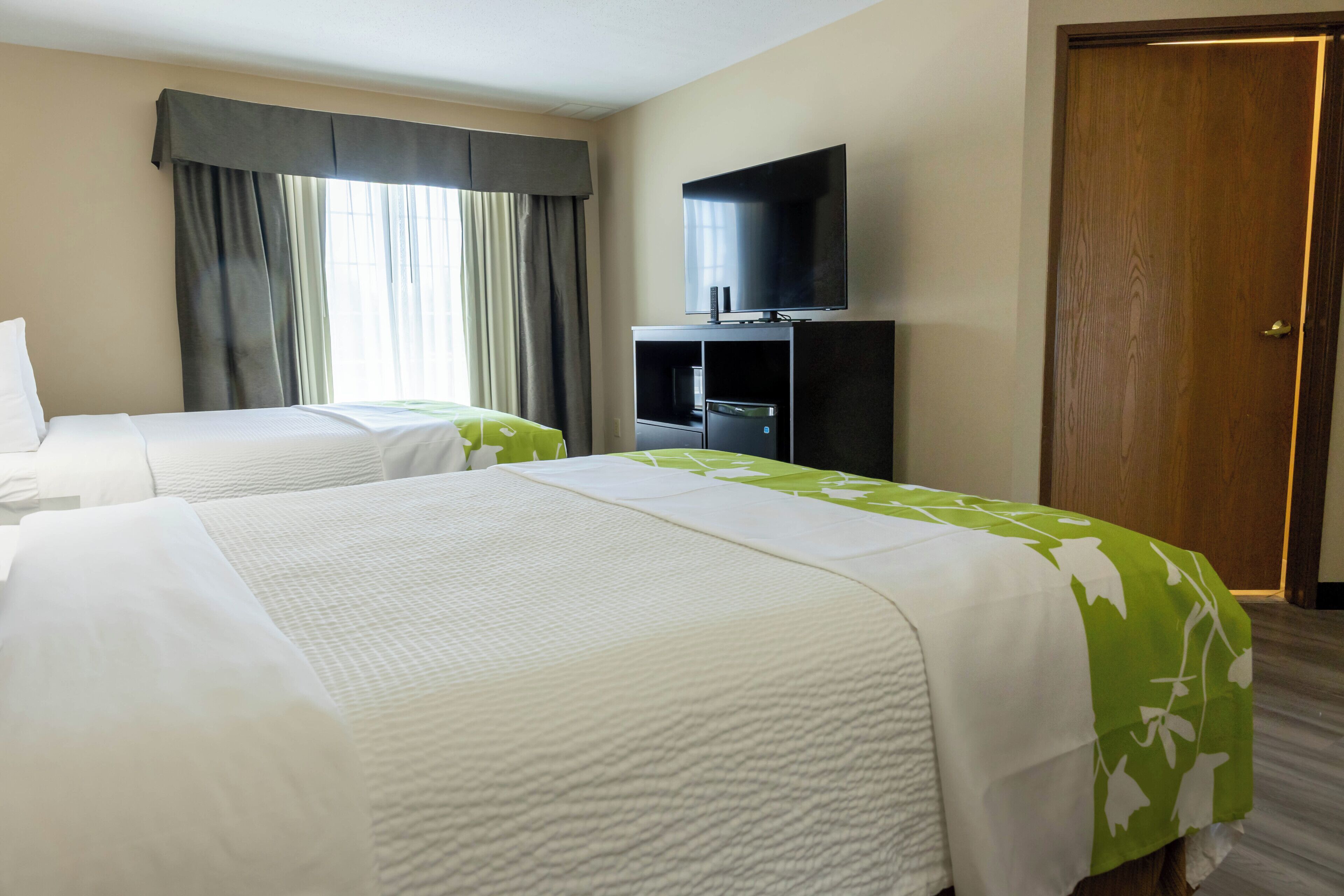 A hotel room with two beds, a television, and a wooden door.
