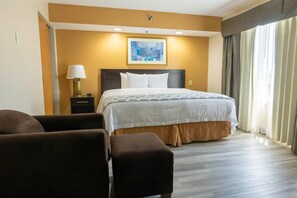 A hotel room with a bed, a nightstand, a lamp, a painting on the wall, and a view of the outdoors through the window. - Wyndham Garden Madison Fitchburg (Madison)