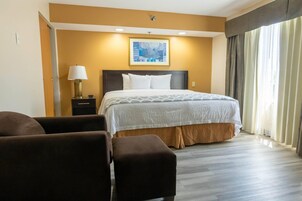 A hotel room with a bed, a nightstand, a lamp, a painting on the wall, and a view of the outdoors through the window.