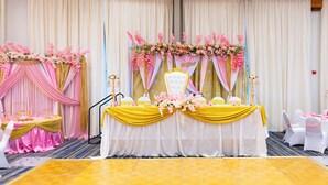 Decoración para una recepción de boda, con escenario, mesas, sillas y arreglos florales.