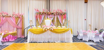 A wedding reception setup with a stage, tables, chairs, and floral decorations.