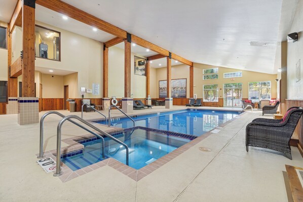 An indoor swimming pool with a tiled floor, wooden beams, and lounge chairs. - Wyndham Garden Madison Fitchburg (Madison)