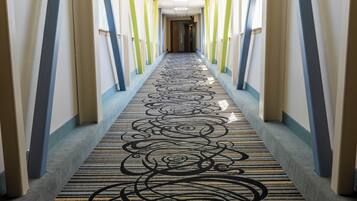 Un couloir d’hôtel avec un tapis à motifs, des colonnes verticales et une porte au fond.