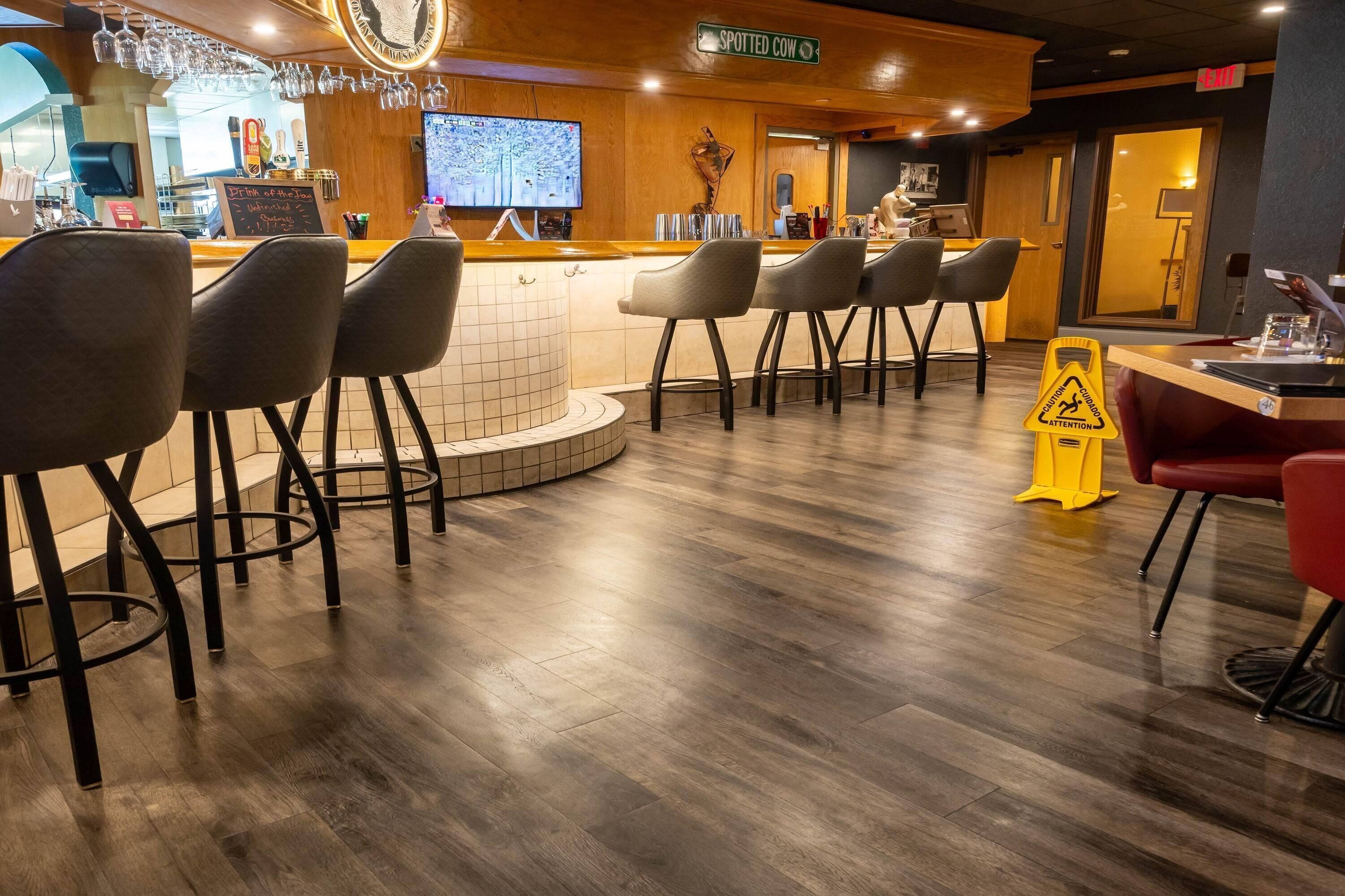 A bar area with stools, a television, and a caution sign on the floor.