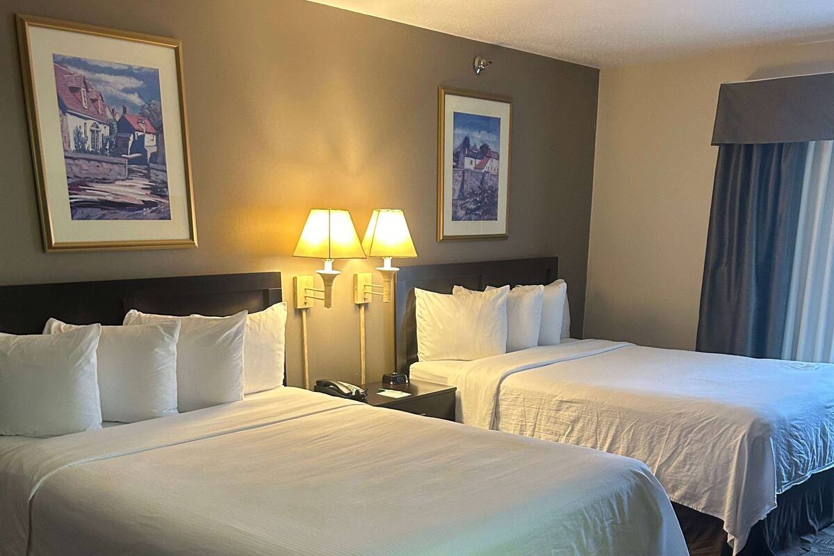 A hotel room with two single beds, a nightstand with a lamp, and two framed pictures on the wall.
