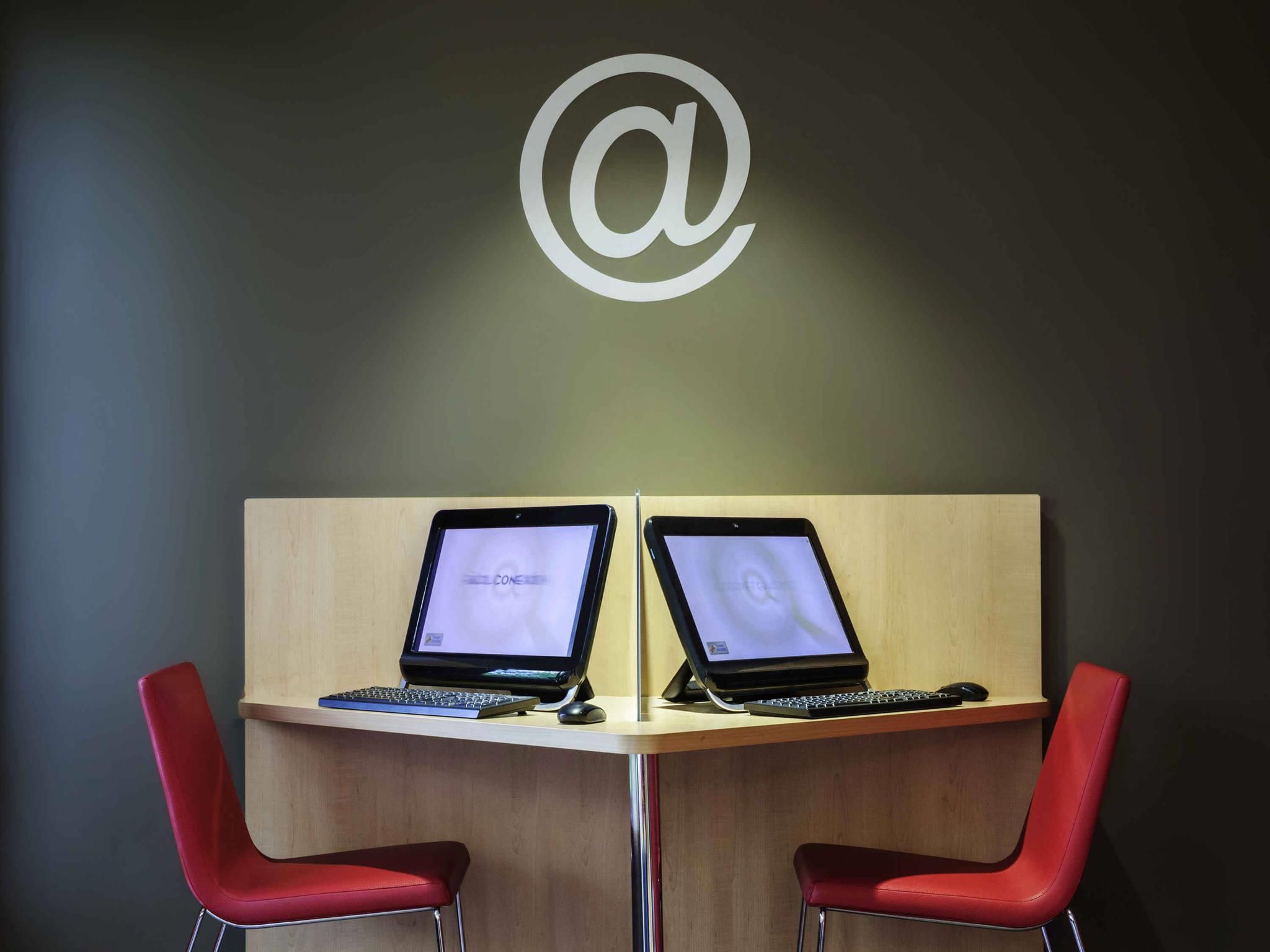 A desk with two laptops, a keyboard, and a mouse, and two red chairs.