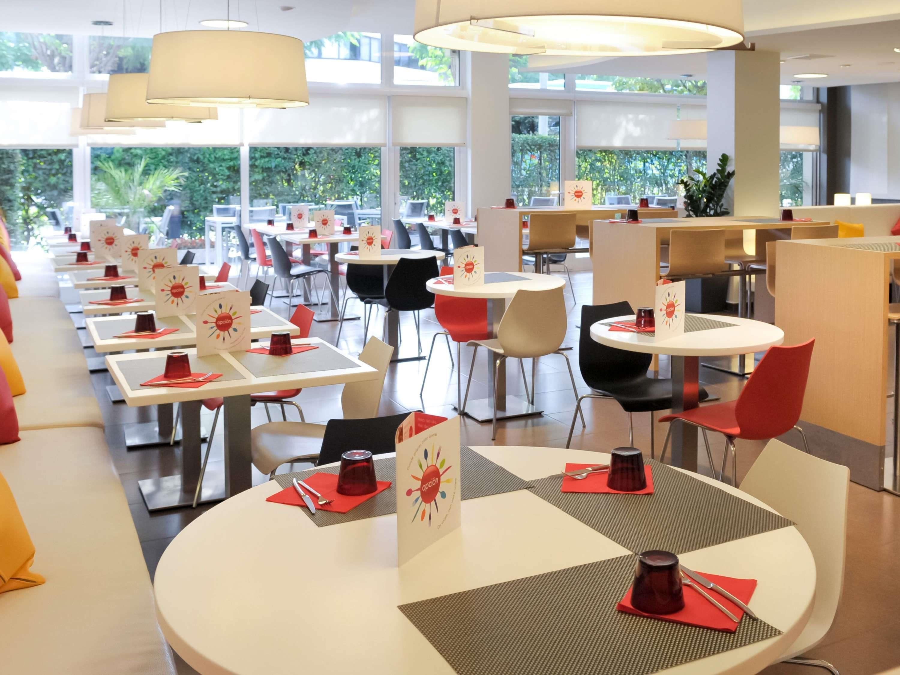 A modern dining area with round tables, red chairs, and pendant lighting.