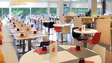 A modern dining area with round tables, red chairs, and pendant lighting.
