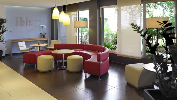 A modern lobby with a curved red sofa, round tables, and pendant lighting. - ibis Barcelona Cornella (Cornella de Llobregat)