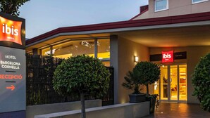 The exterior of the ibis Hotel Barcelona Cornella with a reception area, potted plants, and a clear pathway leading to the entrance. - ibis Barcelona Cornella (Cornella de Llobregat)